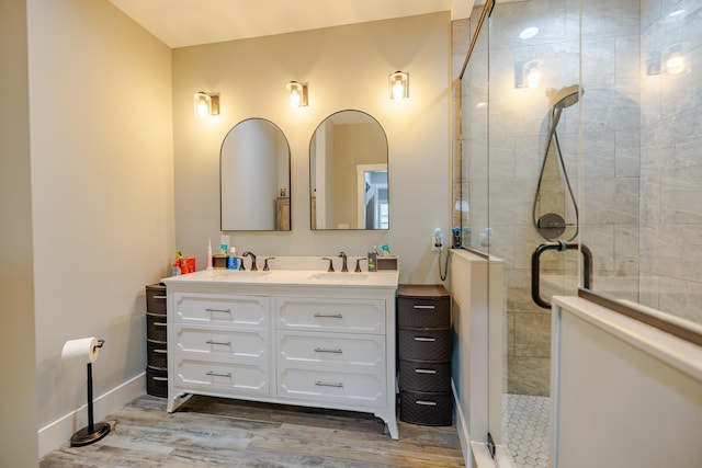 bathroom with double vanity, a stall shower, wood finished floors, and a sink