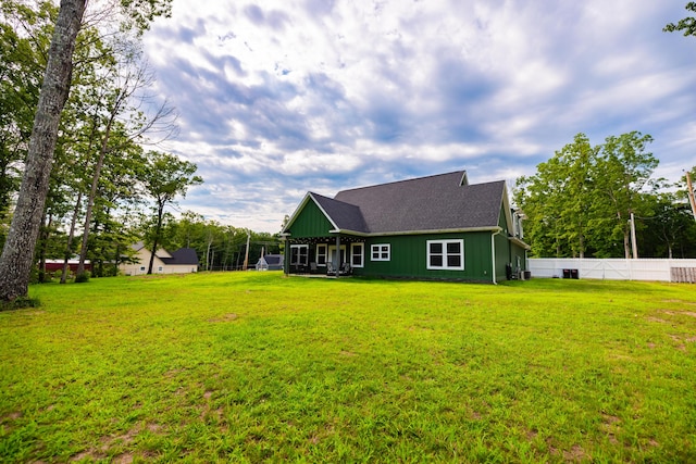 back of house featuring board and batten siding, roof with shingles, a yard, and fence