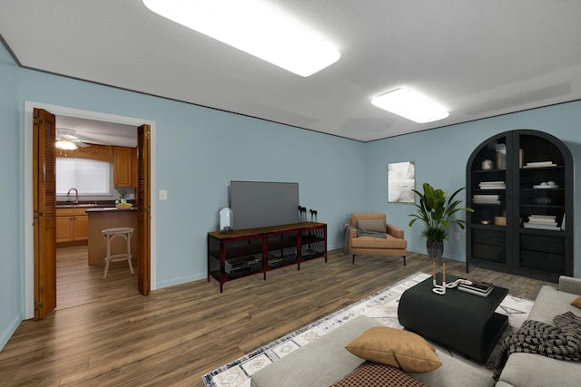 living room with a textured ceiling, ceiling fan, sink, and dark hardwood / wood-style floors