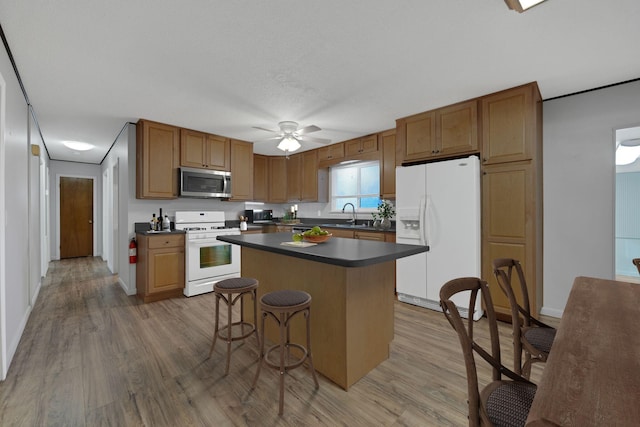 kitchen featuring sink, a center island, white appliances, a breakfast bar area, and light wood-type flooring