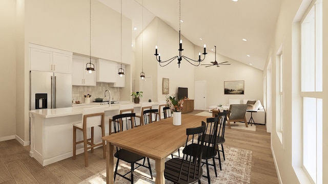 dining room with ceiling fan with notable chandelier, high vaulted ceiling, light wood-type flooring, and sink