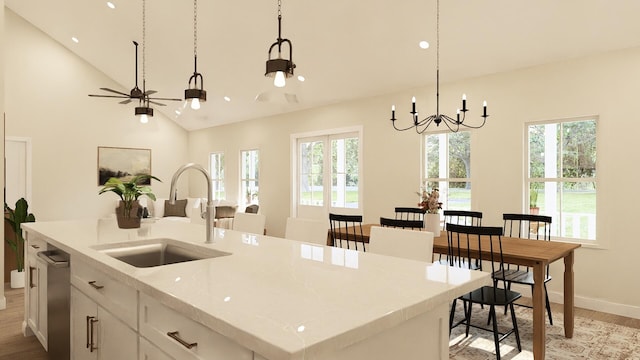 kitchen with light stone countertops, decorative light fixtures, an island with sink, white cabinetry, and sink