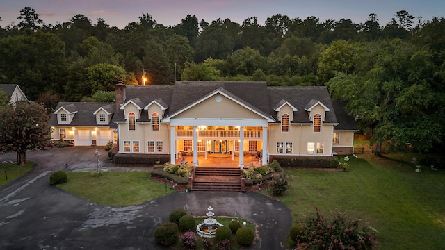 back of house featuring a chimney, curved driveway, stairs, and a lawn