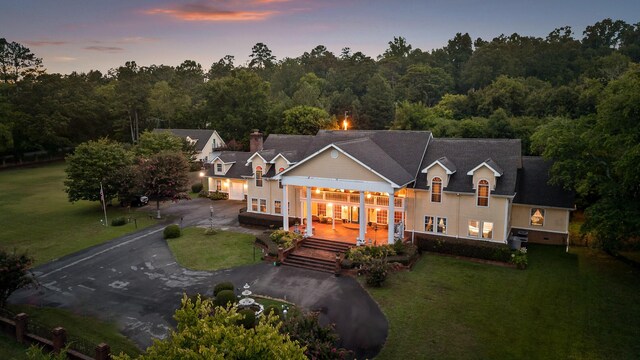 back of property at dusk with a view of trees, driveway, a yard, and a deck