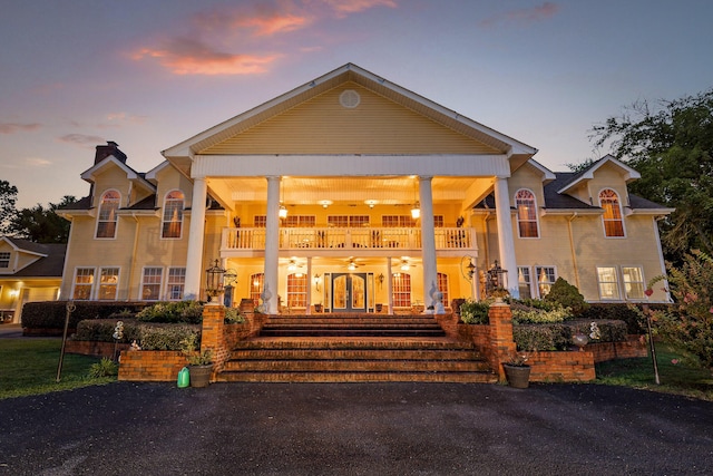 neoclassical home featuring a balcony, a chimney, a porch, and a ceiling fan