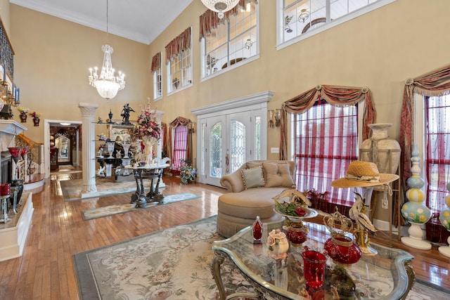 living room with a high ceiling, crown molding, a chandelier, wood-type flooring, and ornate columns