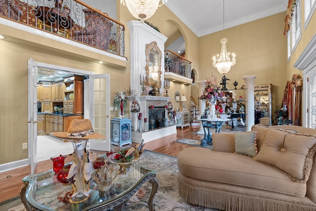 living room with an inviting chandelier, decorative columns, crown molding, hardwood / wood-style flooring, and a towering ceiling