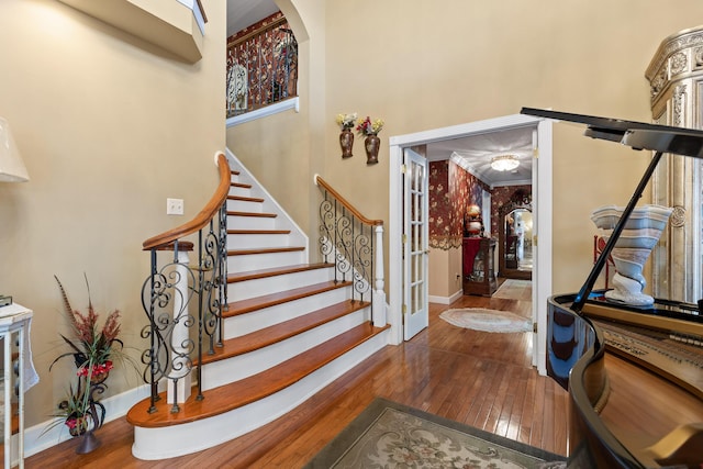 foyer with stairs, a high ceiling, wood-type flooring, baseboards, and arched walkways