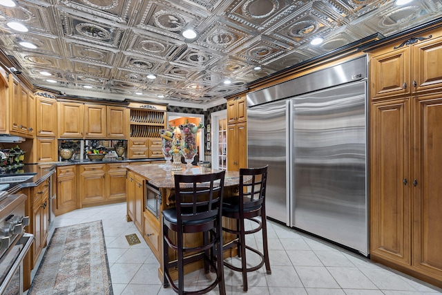 kitchen featuring dark stone countertops, built in appliances, light tile patterned floors, a center island, and sink