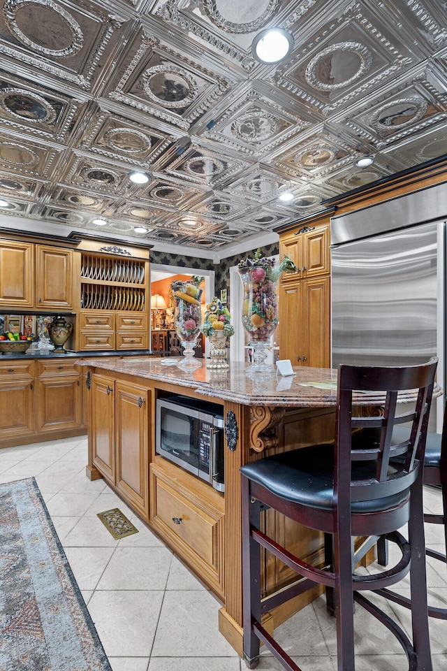 kitchen featuring light tile patterned flooring, an ornate ceiling, brown cabinets, and stainless steel microwave