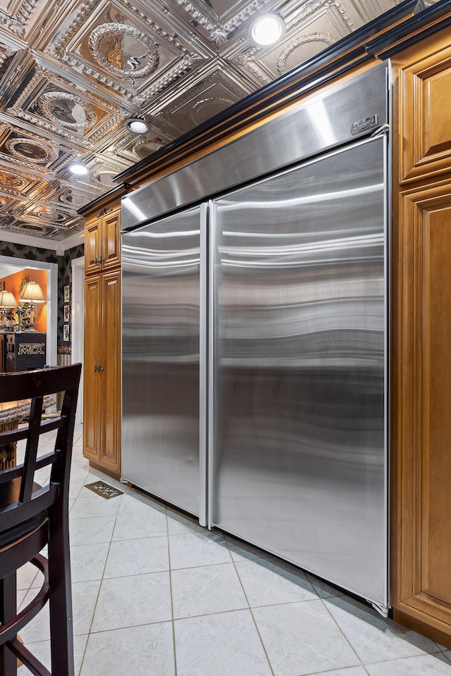 kitchen featuring light tile patterned floors, stainless steel built in fridge, an ornate ceiling, and brown cabinets