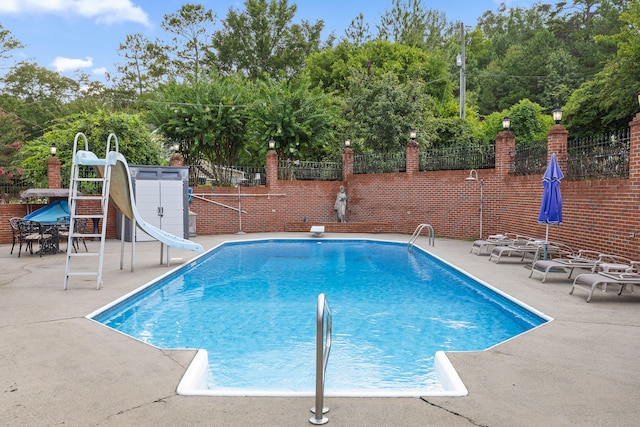 view of pool featuring a water slide, a diving board, and a patio