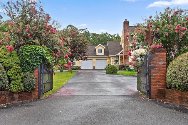view of front of property with driveway, a gate, a garage, and a chimney
