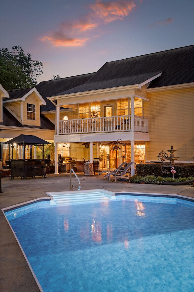 pool at dusk with an outdoor pool and a patio area