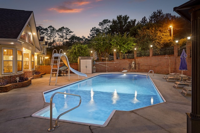 pool at dusk featuring a water slide and a patio area