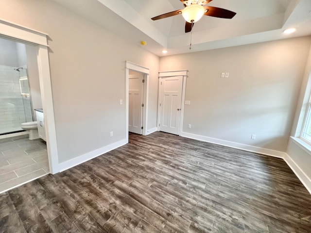 unfurnished bedroom featuring ceiling fan, a tray ceiling, connected bathroom, and dark hardwood / wood-style floors