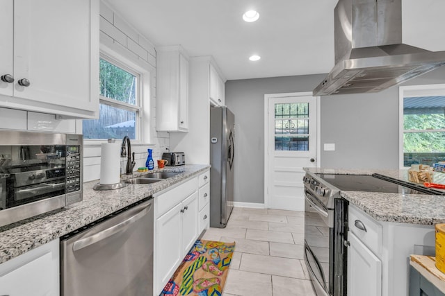 kitchen featuring wall chimney range hood, white cabinetry, a healthy amount of sunlight, and appliances with stainless steel finishes