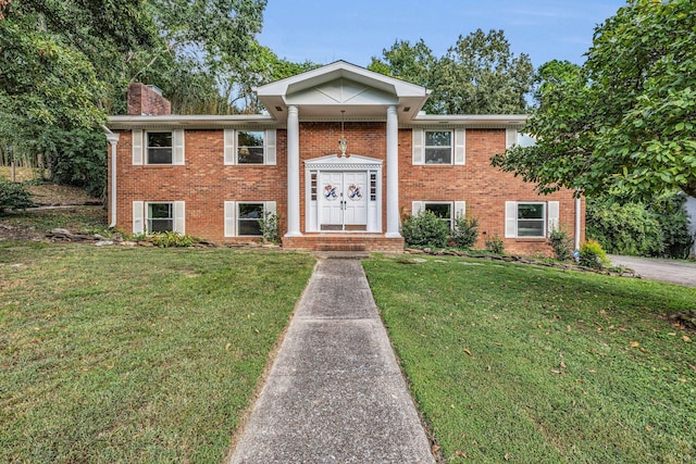 bi-level home with brick siding, a chimney, and a front lawn