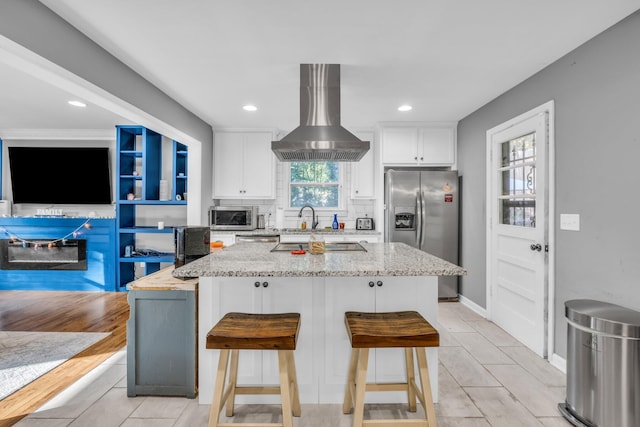 kitchen featuring island range hood, white cabinetry, appliances with stainless steel finishes, light wood-type flooring, and a kitchen breakfast bar