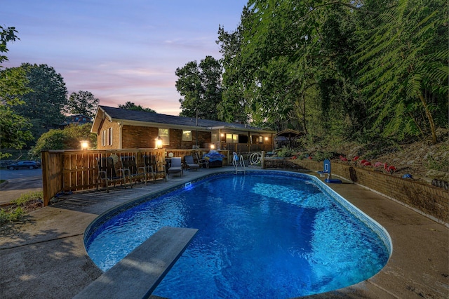 pool at dusk featuring a diving board and a patio