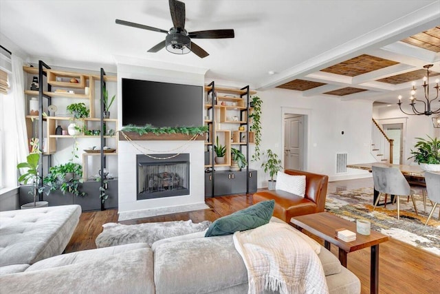 living room with ceiling fan with notable chandelier, beamed ceiling, a tile fireplace, and hardwood / wood-style flooring