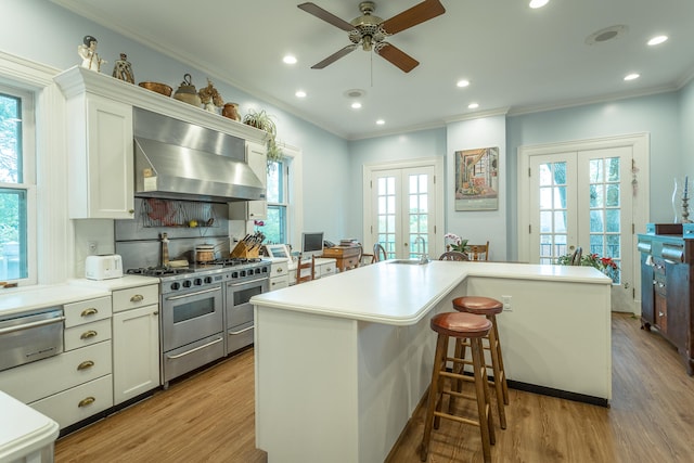 kitchen with a breakfast bar area, french doors, light hardwood / wood-style floors, ceiling fan, and wall chimney range hood