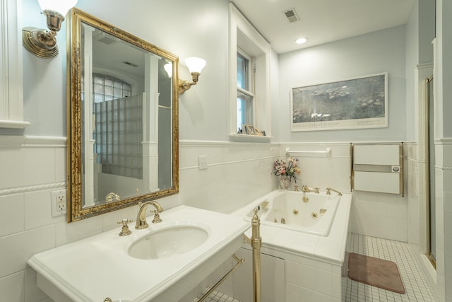 bathroom with tile walls, tile patterned flooring, sink, and tiled bath