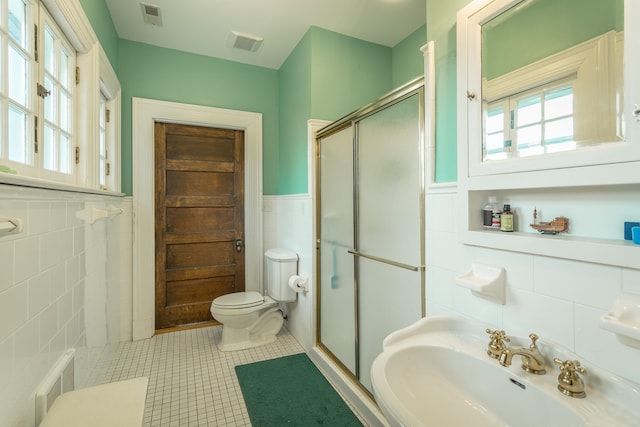 bathroom featuring tile walls, toilet, sink, and a shower with shower door