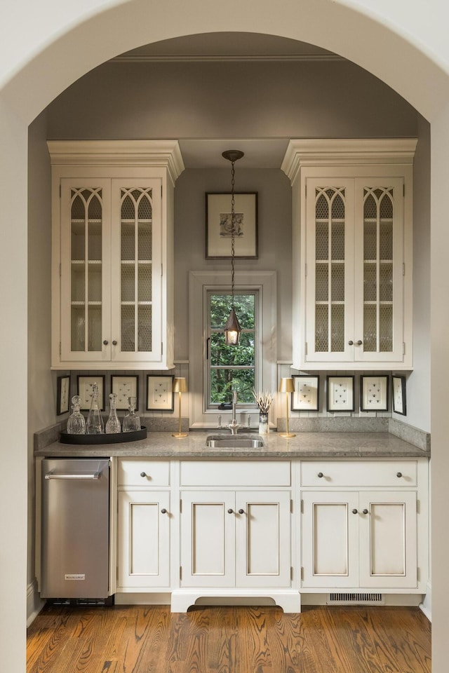 bar with white cabinets, hanging light fixtures, dishwasher, sink, and wood-type flooring