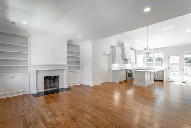 unfurnished living room with light hardwood / wood-style flooring, vaulted ceiling, a notable chandelier, and a fireplace