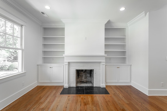 unfurnished living room featuring a fireplace, crown molding, wood-type flooring, and built in shelves