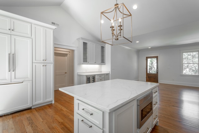 kitchen featuring hardwood / wood-style floors, white cabinetry, decorative light fixtures, a kitchen island, and stainless steel microwave