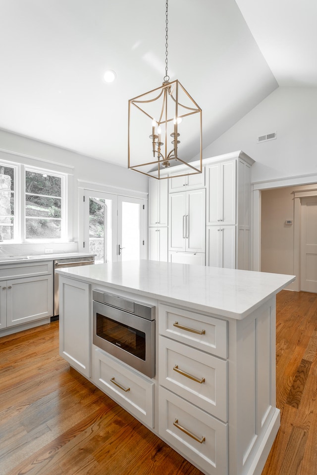 kitchen with vaulted ceiling, light wood-type flooring, pendant lighting, a kitchen island, and stainless steel microwave