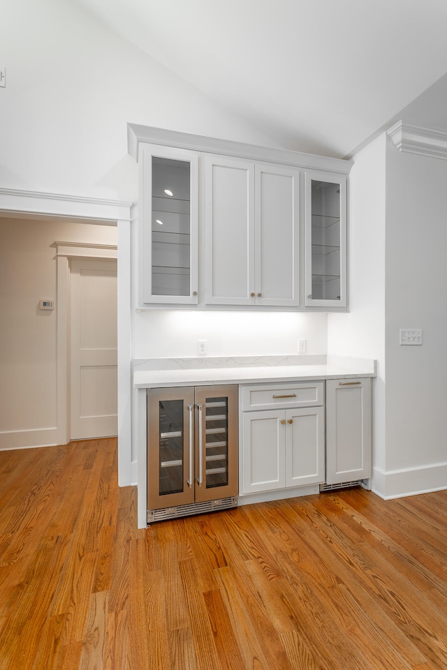 bar featuring light wood-type flooring, white cabinetry, wine cooler, and vaulted ceiling