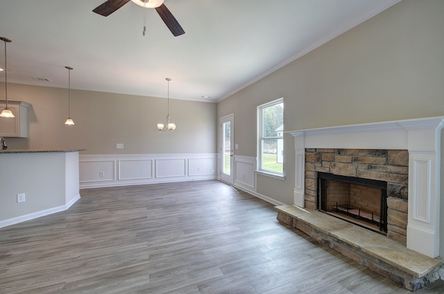 unfurnished living room with crown molding, ceiling fan with notable chandelier, hardwood / wood-style flooring, and a fireplace