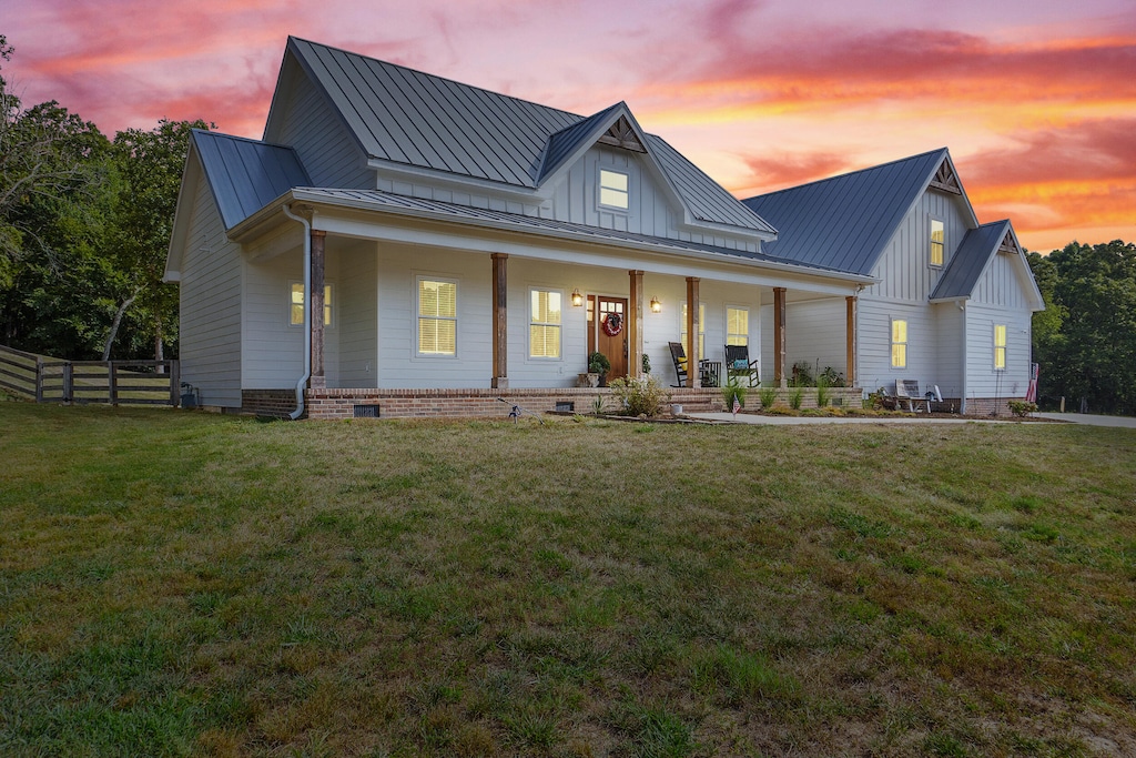 back house at dusk featuring a porch and a lawn