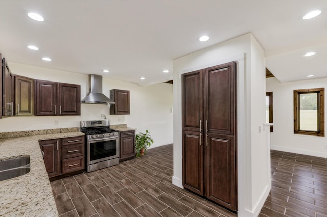 kitchen with light stone countertops, wall chimney range hood, stainless steel gas range, dark brown cabinets, and dark wood-type flooring