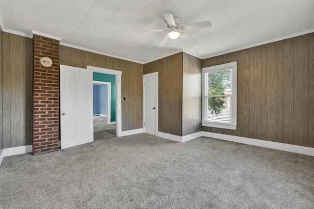 unfurnished bedroom featuring carpet flooring, ceiling fan, crown molding, and wood walls