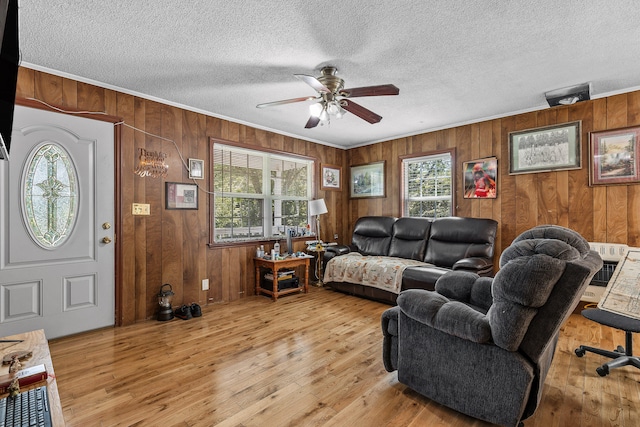 living room with crown molding, a textured ceiling, light hardwood / wood-style flooring, wood walls, and ceiling fan