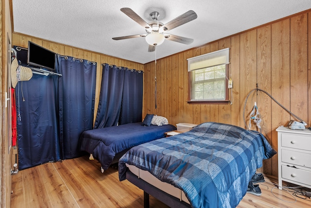 bedroom with a textured ceiling, ceiling fan, wood walls, and light hardwood / wood-style floors