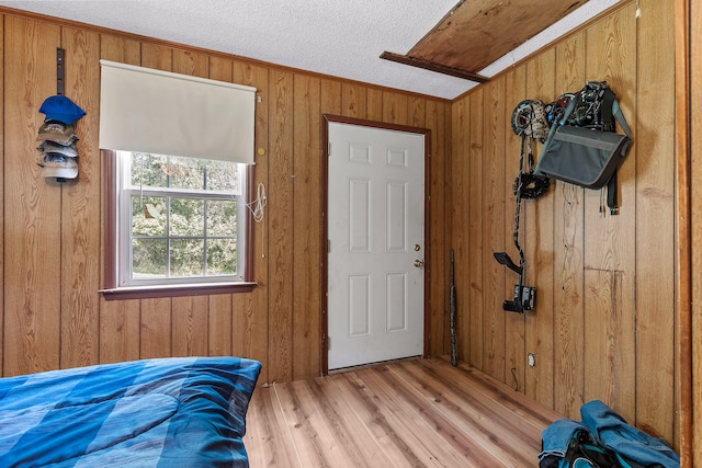 bedroom with light wood-type flooring, crown molding, a textured ceiling, and wooden walls