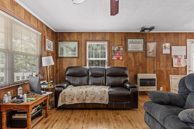 living room featuring wooden walls, ornamental molding, a textured ceiling, light hardwood / wood-style flooring, and heating unit