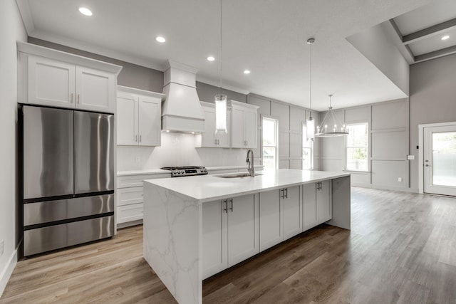 kitchen with appliances with stainless steel finishes, a center island with sink, custom range hood, and light hardwood / wood-style flooring