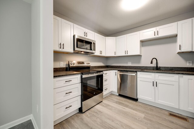 kitchen featuring light wood-type flooring, dark stone counters, white cabinetry, sink, and appliances with stainless steel finishes