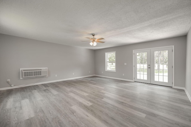 empty room featuring a wall unit AC, french doors, light hardwood / wood-style floors, ceiling fan, and a textured ceiling