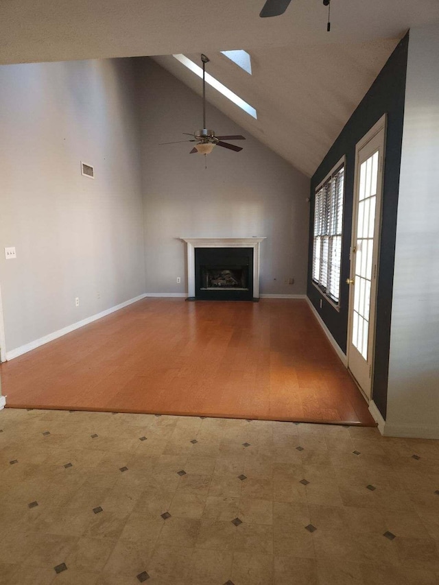 unfurnished living room featuring ceiling fan, a skylight, and high vaulted ceiling