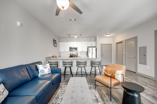 living room with light wood-type flooring, ceiling fan, electric panel, and sink