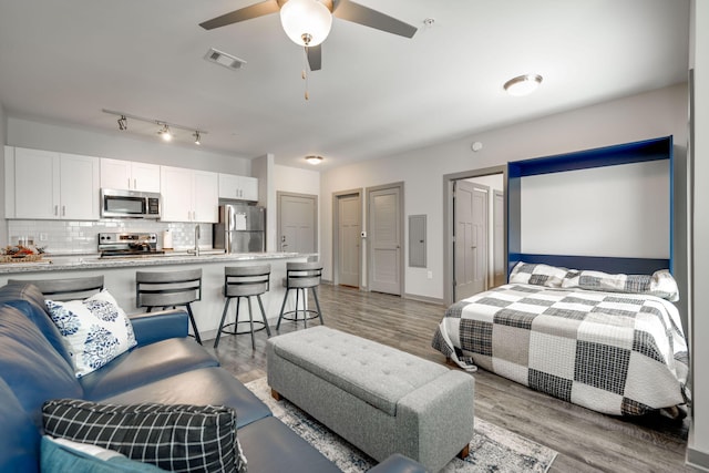 bedroom with electric panel, light hardwood / wood-style floors, stainless steel refrigerator, sink, and ceiling fan