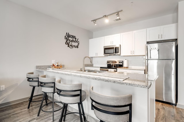 kitchen with sink, appliances with stainless steel finishes, white cabinetry, and light hardwood / wood-style floors