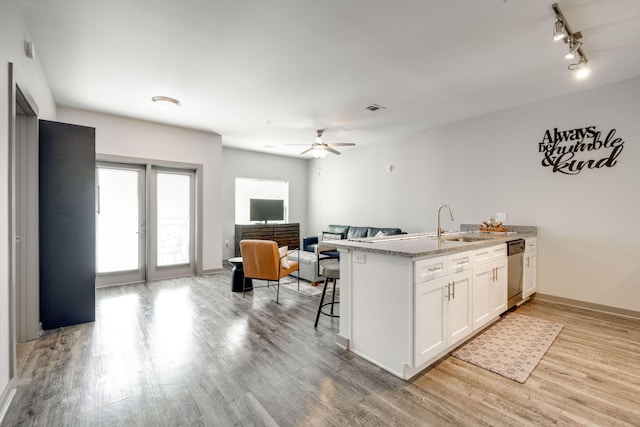 kitchen with light hardwood / wood-style flooring, stainless steel dishwasher, a breakfast bar, ceiling fan, and white cabinets